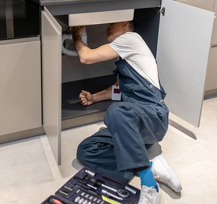 Handwerker unter einer Küchenspüle, der dort den Siphon anbringt.