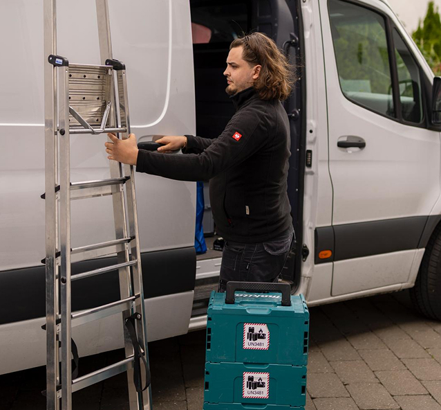 Monteur, der sein Montageequipment in einen weißen Transporter einräumt.