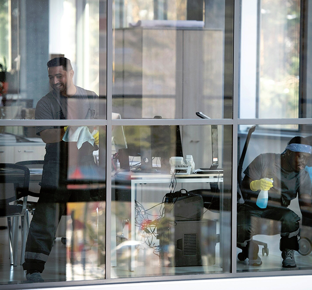 Zwei Reinigungskräfte beim putzen von Glasscheiben in einem Büro